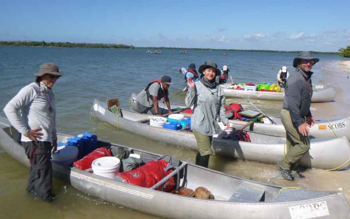 participants stand beside canoes resting on a beach on a family expedition with outward bound